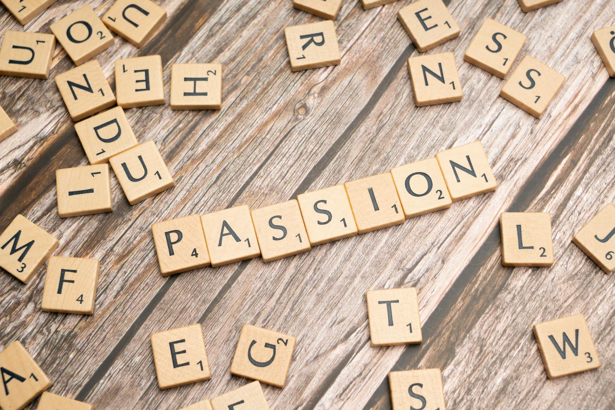Wooden letter tiles forming the word 'PASSION' on a wooden background, symbolizing creativity and motivation.